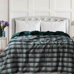 a bed with white pillows and green plaid comforter on it, next to a lamp