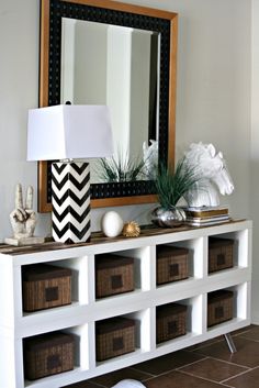 a white shelf with some baskets and a lamp on it next to a large mirror