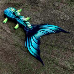 a blue and black fish laying on top of the sand with its tail curled up