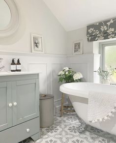 a white bath tub sitting under a window next to a sink in a bathroom filled with flowers