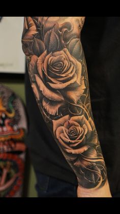 a man's arm with roses and leaves tattooed on the forearm, in black and grey