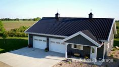 an aerial view of a two story house with a black metal roof and white garage doors