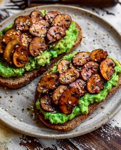 two pieces of bread with avocado and mushrooms on it sitting on a plate