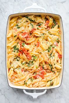 a casserole dish filled with pasta, tomatoes and spinach on a marble surface