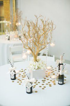 a white table topped with vases filled with flowers and candles next to a tree