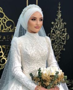 a woman in a white wedding gown and veil holding a bouquet of flowers with her hands