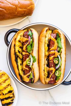 two hot dogs with toppings in a pan next to a grilled pineapple