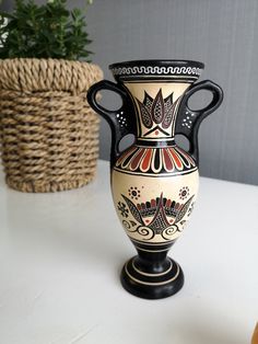 a black and white vase sitting on top of a table next to a potted plant