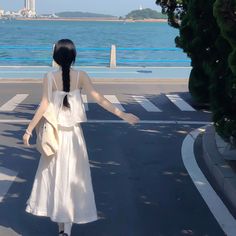 a woman walking across a street next to the ocean with her arms spread wide open