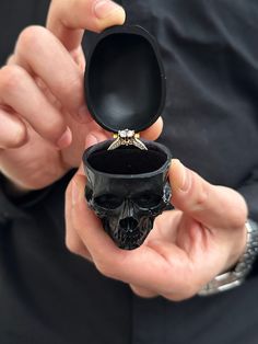 a person holding an open ring box with a skull in it's middle,