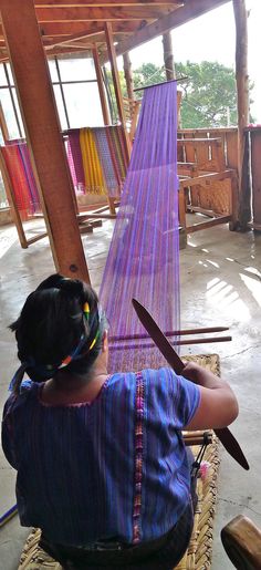 a woman sitting in front of a weaving machine holding a large pair of scissors next to it