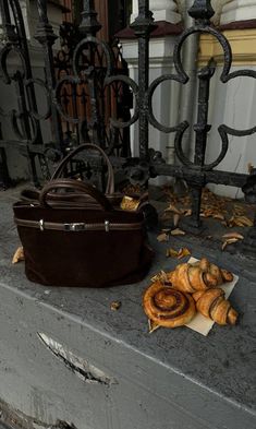 a brown bag sitting on top of a cement bench next to a pile of croissants