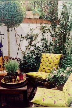 an outdoor living area with yellow and green furniture, potted plants and flowers on the table