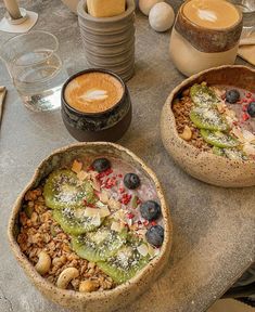 two bowls filled with food sitting on top of a table next to cups of coffee