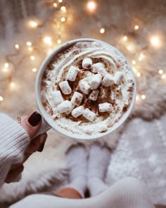 someone holding a cup of hot chocolate with marshmallows on top