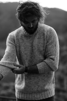 a man with long hair wearing a sweater and holding a wine glass in his hand