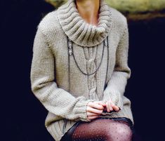 a woman sitting on top of a wooden bench wearing a sweater and tights with her hands in her pockets