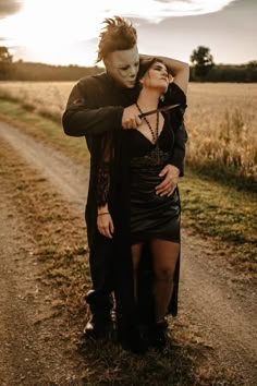 a man and woman dressed up in costumes standing on a dirt road with the sun behind them