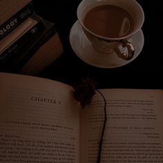 an open book next to a cup of coffee on a saucer and stack of books