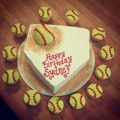 a birthday cake with softballs around it on a wooden table next to cupcakes