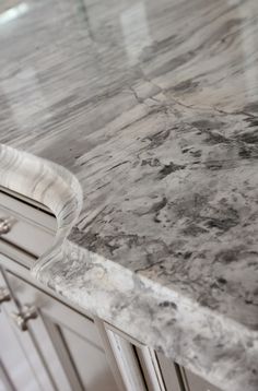 a marble counter top in a kitchen with white cupboards and drawers on either side