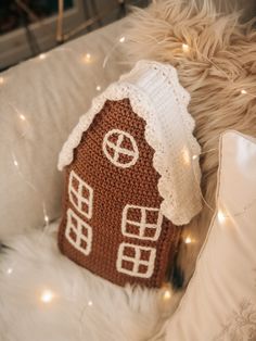 a crocheted gingerbread house pillow on a white couch with christmas lights around it