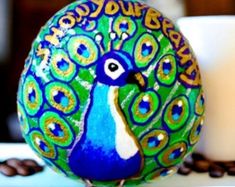 a peacock painted on an egg next to coffee beans