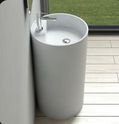 a white sink sitting next to a window on top of a tiled floor in front of a grass covered field