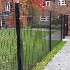 a black metal fence next to a brick building with green grass and trees in the background