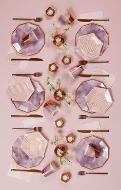 the table is set with pink plates, silverware and flowers on top of them