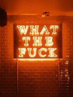 a neon sign that reads, what the fock? on a brick wall in a dark room