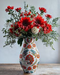 a vase filled with red and white flowers on top of a wooden table next to a wall