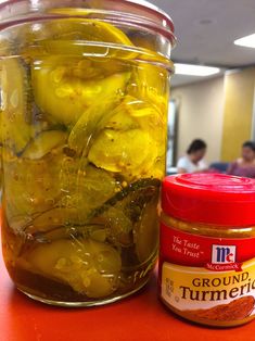 a jar filled with pickles sitting on top of a table next to a jar of mustard