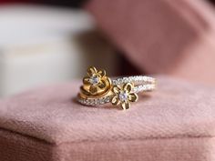 two gold and diamond rings sitting on top of a pink cushion