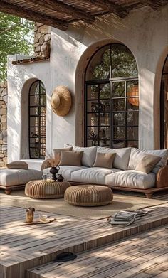 an outdoor living room with white couches and pillows on the floor next to large windows