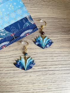 two pairs of earrings sitting on top of a wooden table next to a blue box