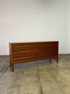 a large wooden dresser sitting on top of a cement floor next to a white brick wall