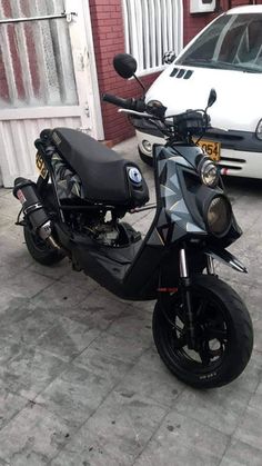 a motorcycle parked next to a white car on a brick sidewalk in front of a building