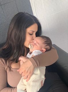 a woman holding a baby in her arms and kissing it's face with the other hand