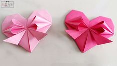 two pink origami hearts sitting on top of a white table next to each other