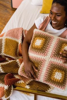 a woman is smiling while holding a crocheted pillow