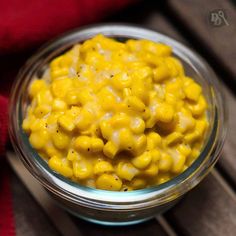 a glass bowl filled with corn on top of a wooden table