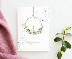 a christmas card with a candle on it next to a plant and a pink sweater