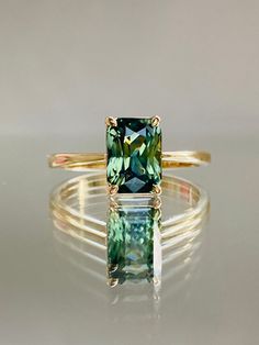 a gold ring with an emerald colored stone in the center and two thin bands around it