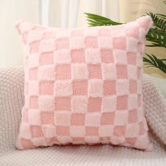 a pink and white checkered pillow sitting on top of a couch next to a potted plant