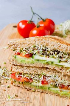 a cut in half sandwich sitting on top of a wooden cutting board next to tomatoes