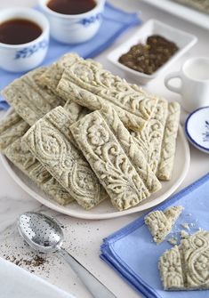 some cookies are on a white plate with blue napkins and two cups of tea