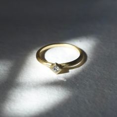 a gold ring with a single diamond in the center on a white surface, casting a shadow