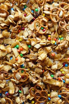 a pile of cereal with m & ms on top and candy in the middle, as well as pretzels