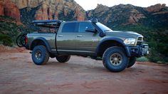 a large truck parked on top of a dirt field next to some rocks and trees